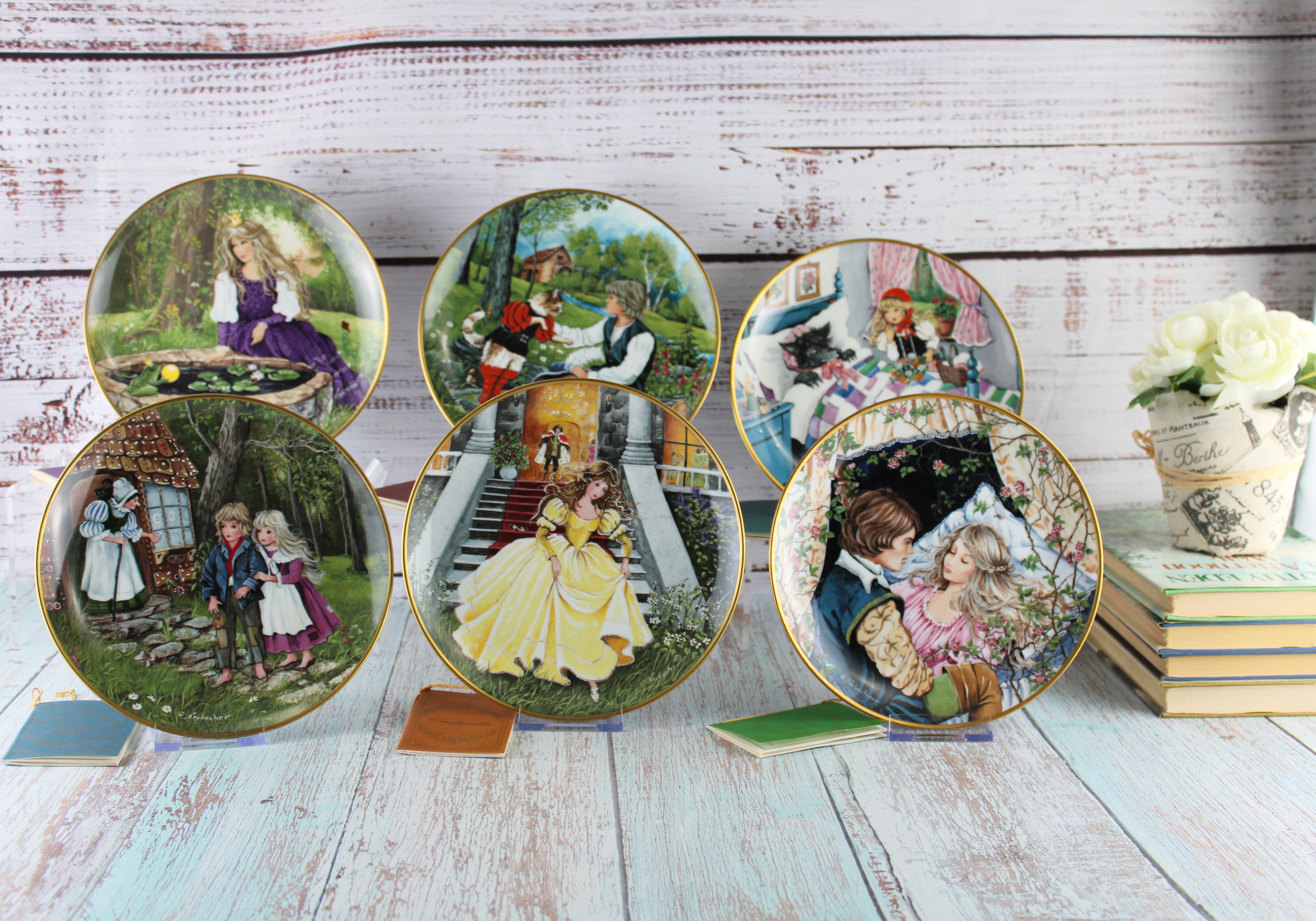 Collection of decorative illustrated plates displayed with books and a flower